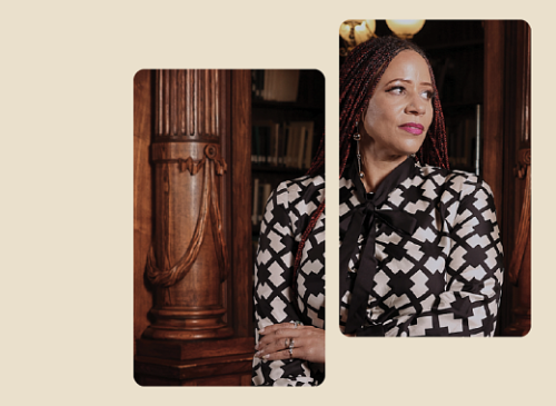 A person with braided hair and patterned blouse stands in front of a wooden column, looking to the side.