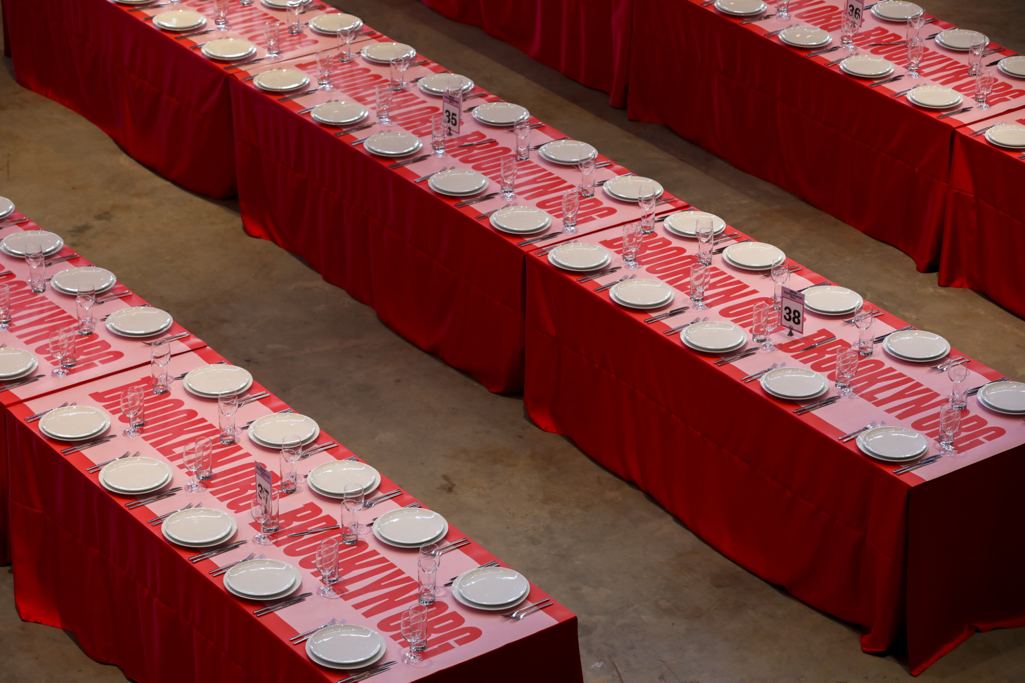 Rows of banquet tables with red tablecloths and place settings arranged neatly with plates, glasses, and cutlery.