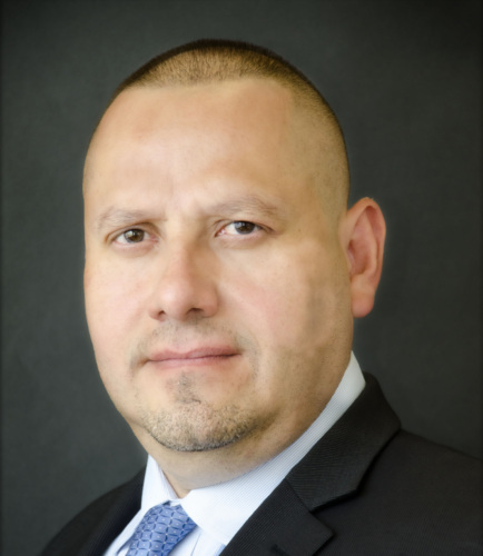 A man in a suit and tie poses against a dark background, looking directly at the camera.