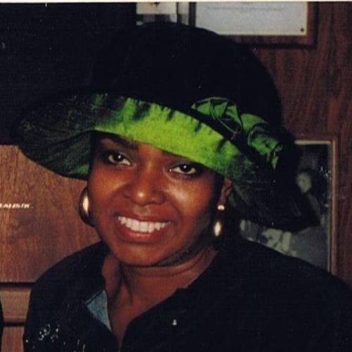 Person wearing a green and black hat and gold hoop earrings smiles at the camera.