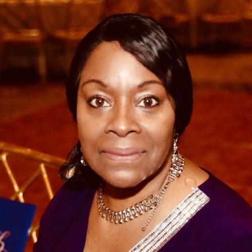 A person in a blue dress is sitting at a table in a banquet hall, holding a pen.