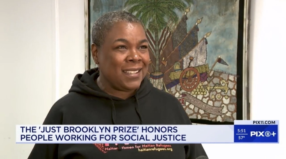 Person speaking in a news interview, standing in front of a painting, with a headline about the 'Just Brooklyn Prize' honoring social justice work.