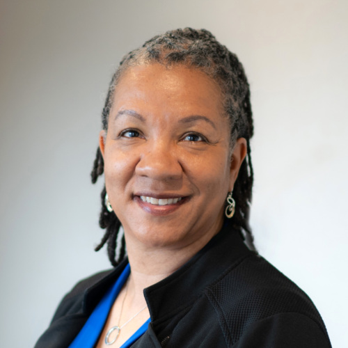 Person smiling, wearing a black jacket and blue shirt, with a neutral background.