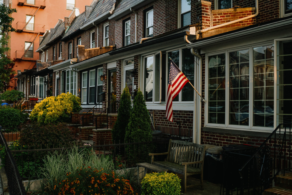 Row of brick houses with large windows and a garden. An American flag is displayed on one of the houses.