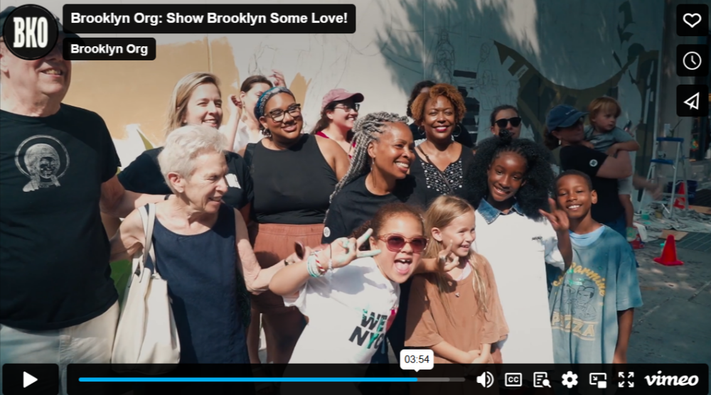 A group of people, including adults and children, are smiling and posing outdoors for a photo.