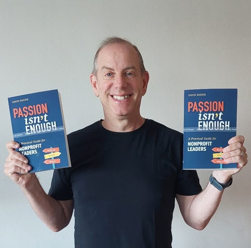 Person holding two copies of a book titled "Passion Isn't Enough: A Practical Guide for Nonprofit Leaders" while smiling, wearing a black shirt.