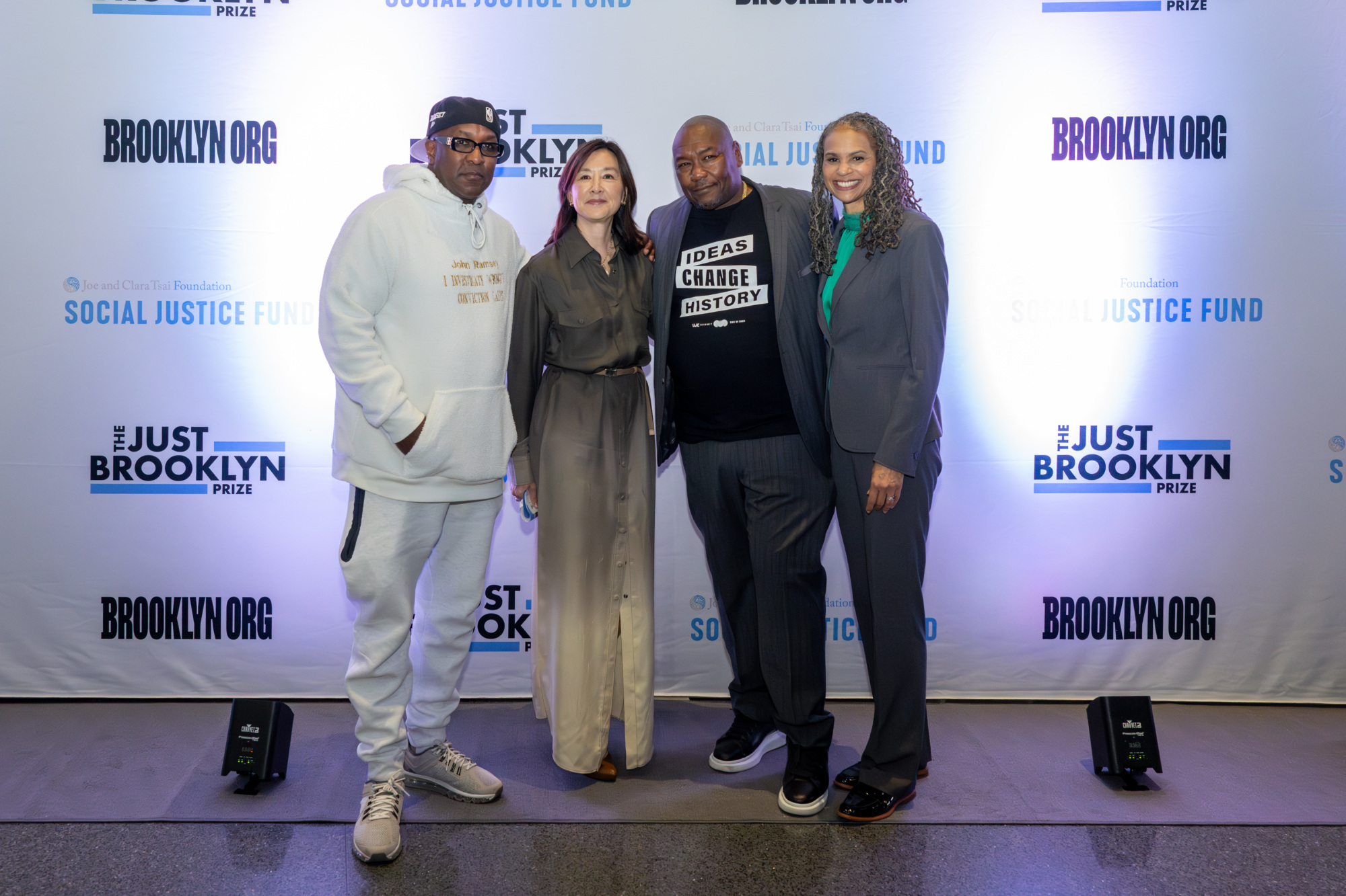 Four people stand together on a red carpet at an event, posing in front of a backdrop with "Brooklyn.org" and "Social Justice Fund" logos.