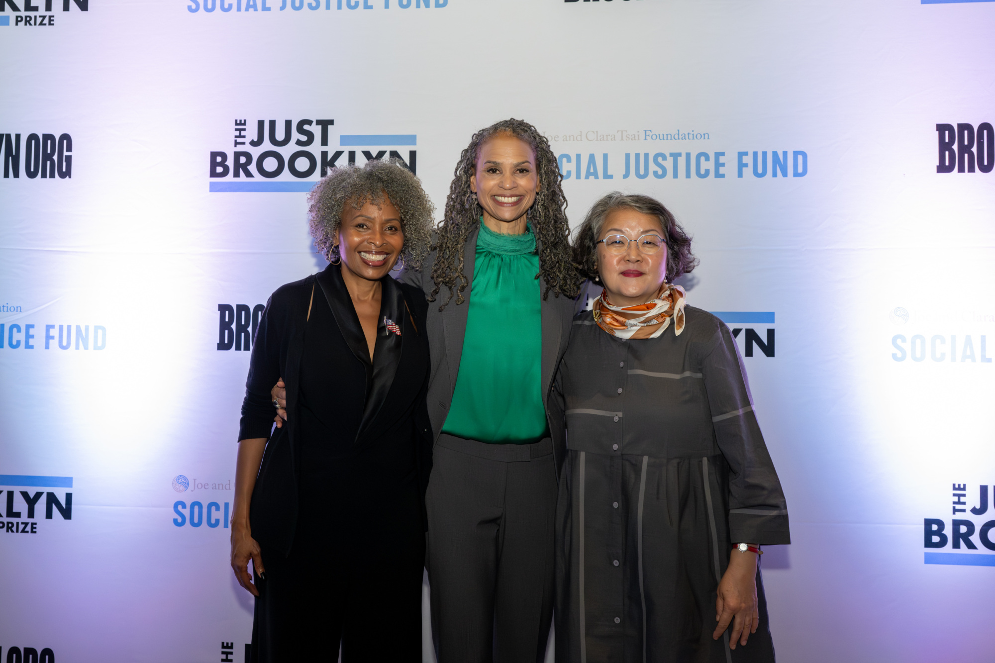 Three individuals smiling, standing in front of a backdrop with "The Just Brooklyn Prize" and "Social Justice Fund" logos.