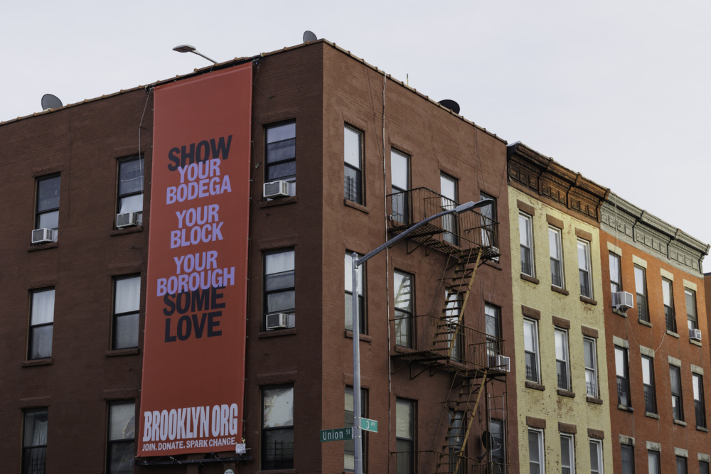 A large banner on a brick building reads, "Show your bodega, your block, your borough some love." It is located at the corner of Union Street.