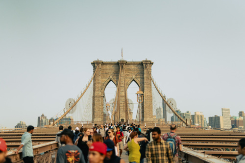 People walking on the Brooklyn Bridge with the New York City skyline in the background.