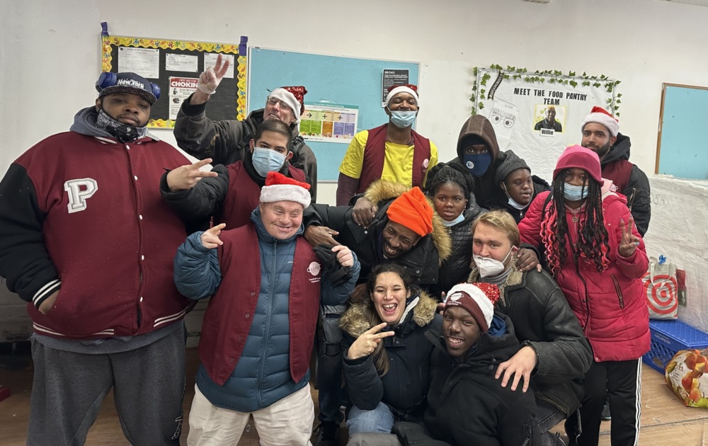 A group of people, some wearing Santa hats, pose together indoors. They are standing in front of a wall with posters.