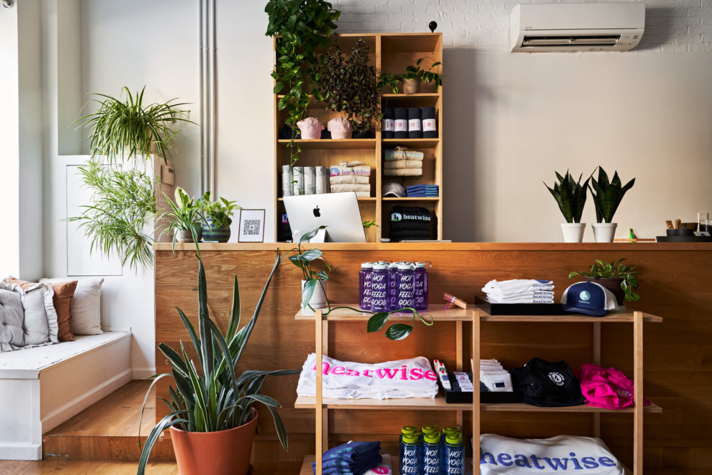 A retail display area featuring shelves with branded merchandise, plants, and an iMac on a wooden counter in a well-lit, modern interior.