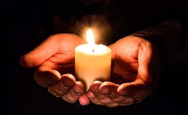 Hands cupping a lit candle in a dark setting.