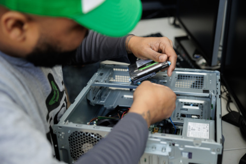 Person in a green cap installing a hard drive inside a computer case on a desk.