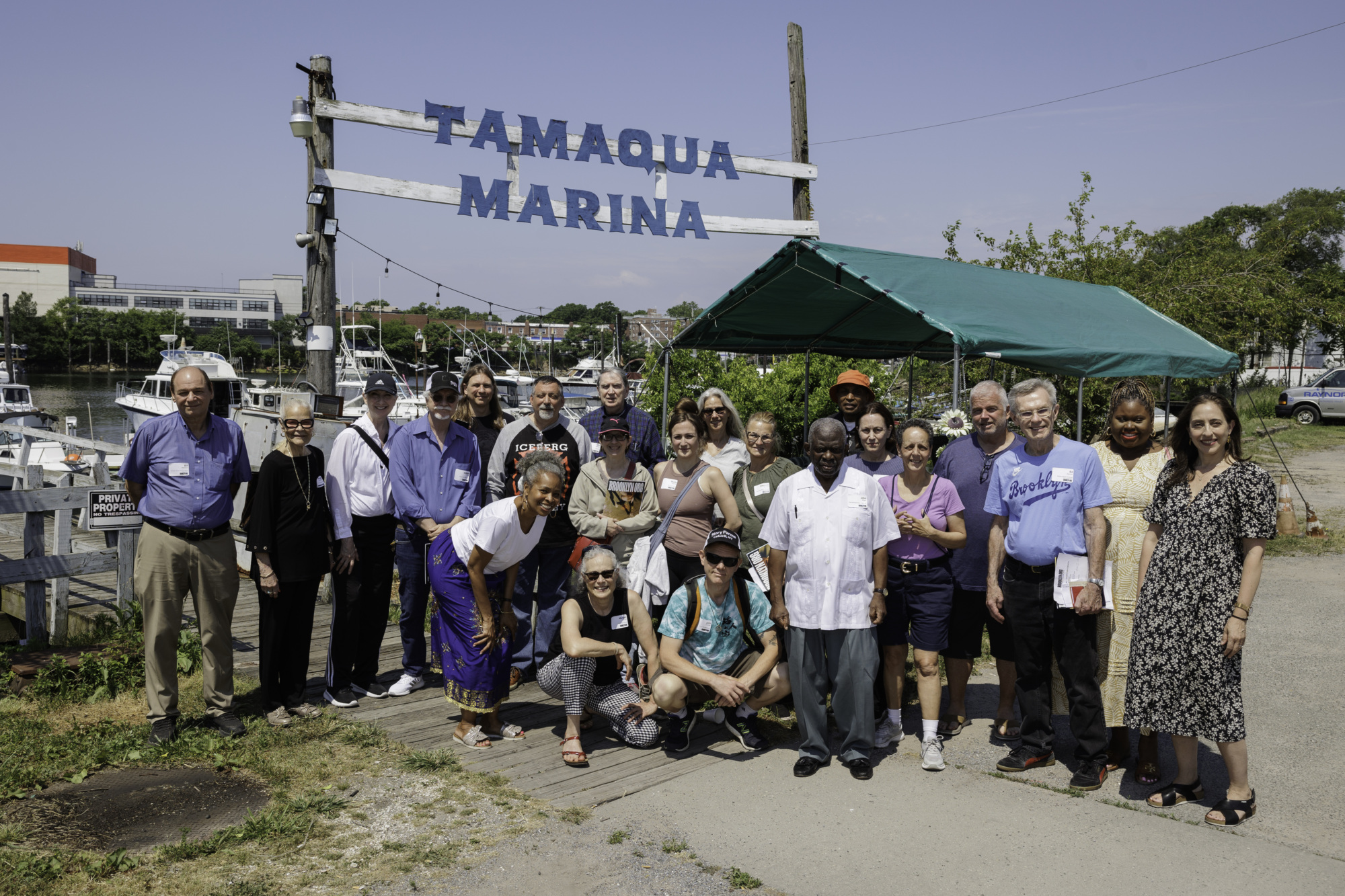 A group of people posing in front of a sign that reads "Tamaqua Marina." They are standing under a clear sky near a small, green tent.