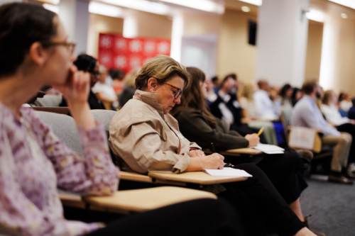 People seated in a lecture hall, taking notes and listening attentively.