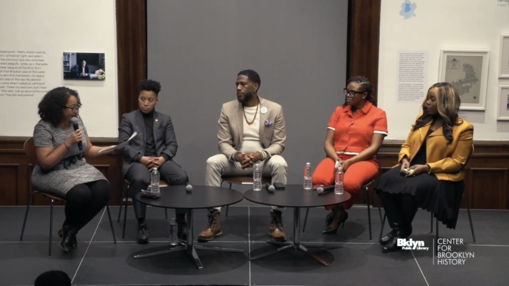 Five people sit on a stage panel discussion at the Center for Brooklyn History. Four are on chairs, and one is speaking into a microphone.