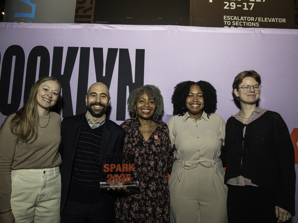 A group of five people standing together in front of a purple banner, one person holding a "Spark 2023" award.