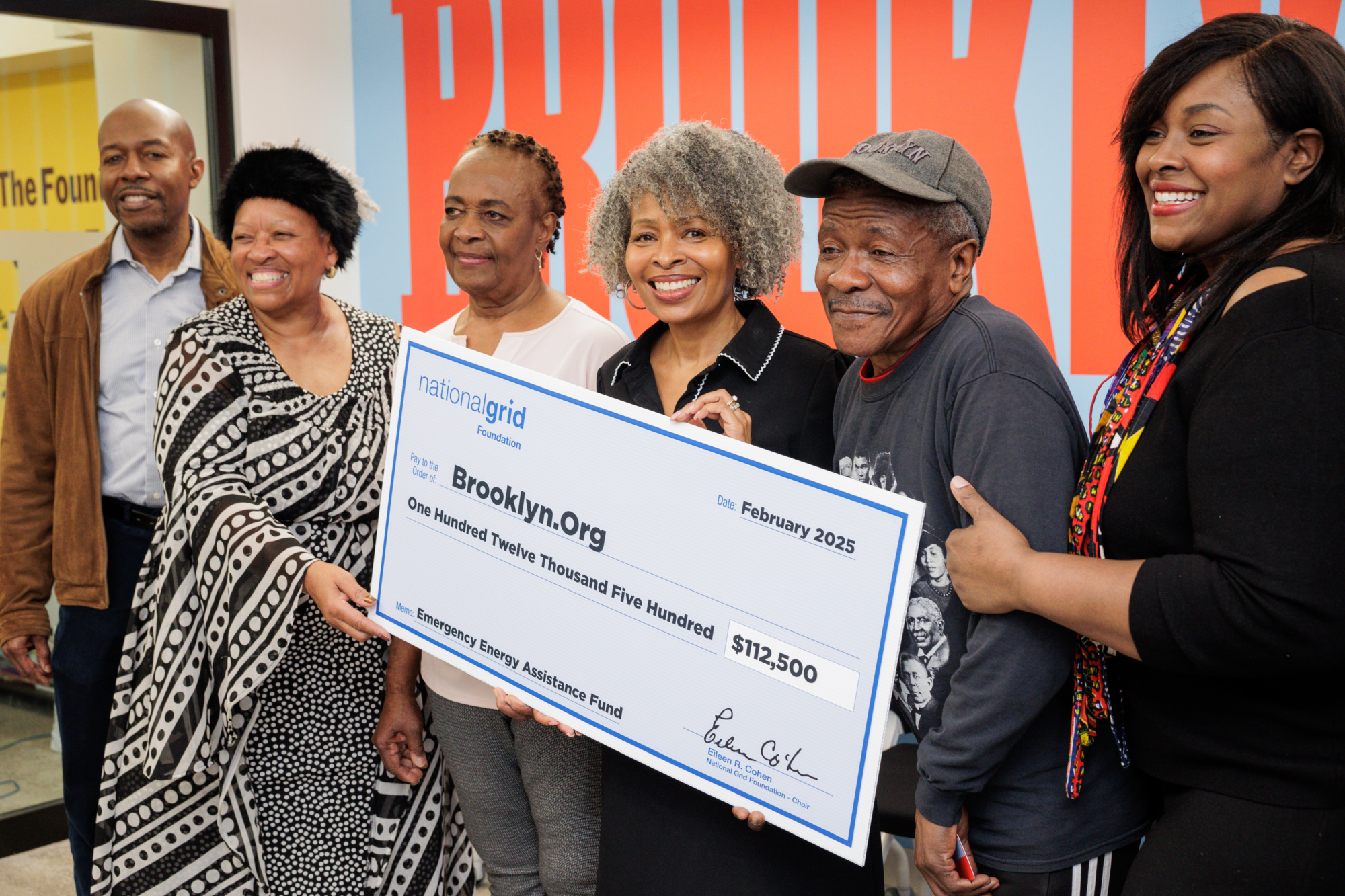 A group of six people stand together, holding a large check for $112,500 made out to Brooklyn.Org from National Grid. The check is dated February 2025.