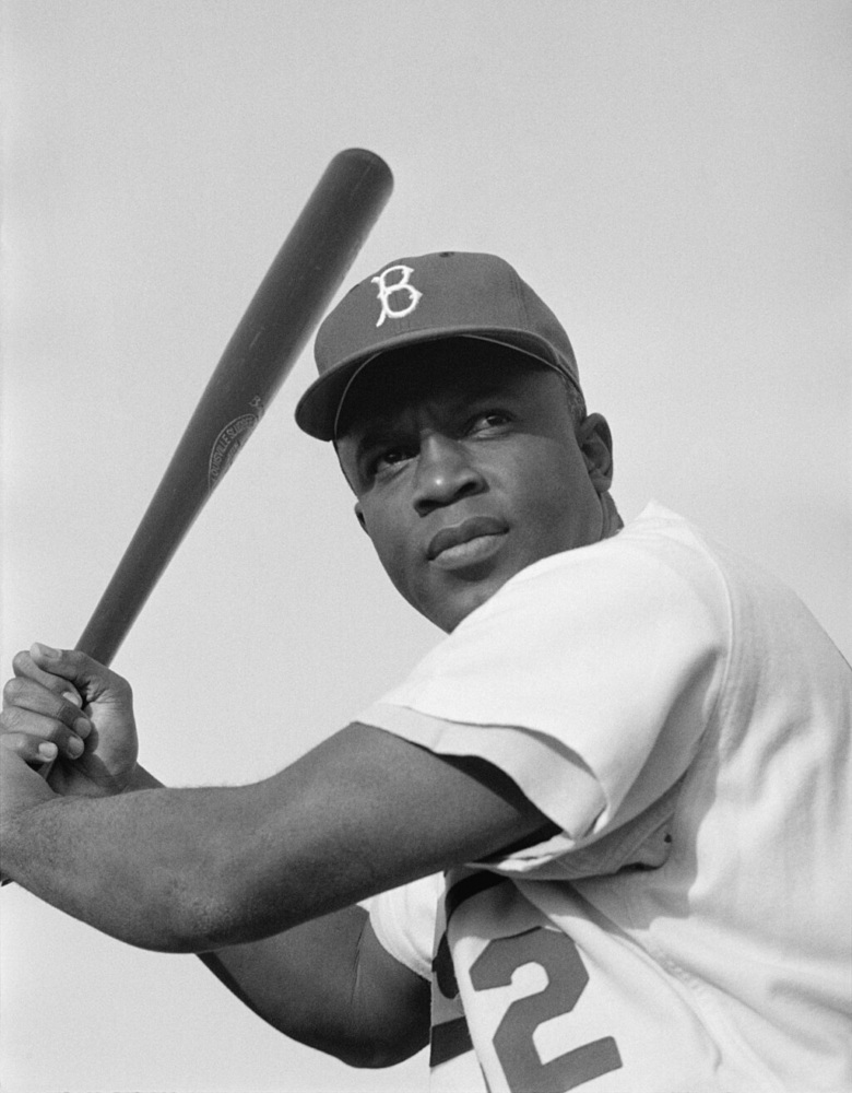 A baseball player in a Brooklyn Dodgers uniform holds a bat, poised to swing.