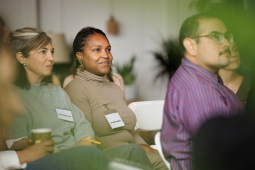 A group of people sitting and attentively listening in a room, with some wearing name tags.
