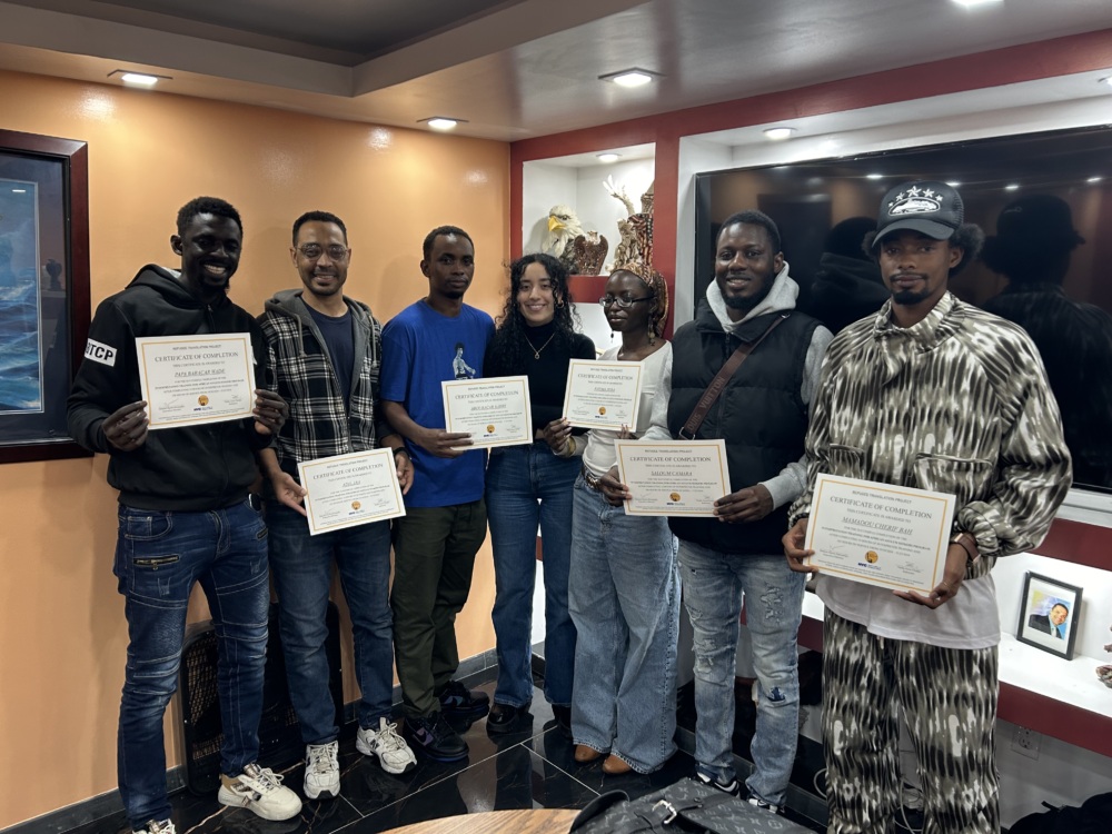 Seven people standing indoors holding certificates, smiling at the camera.