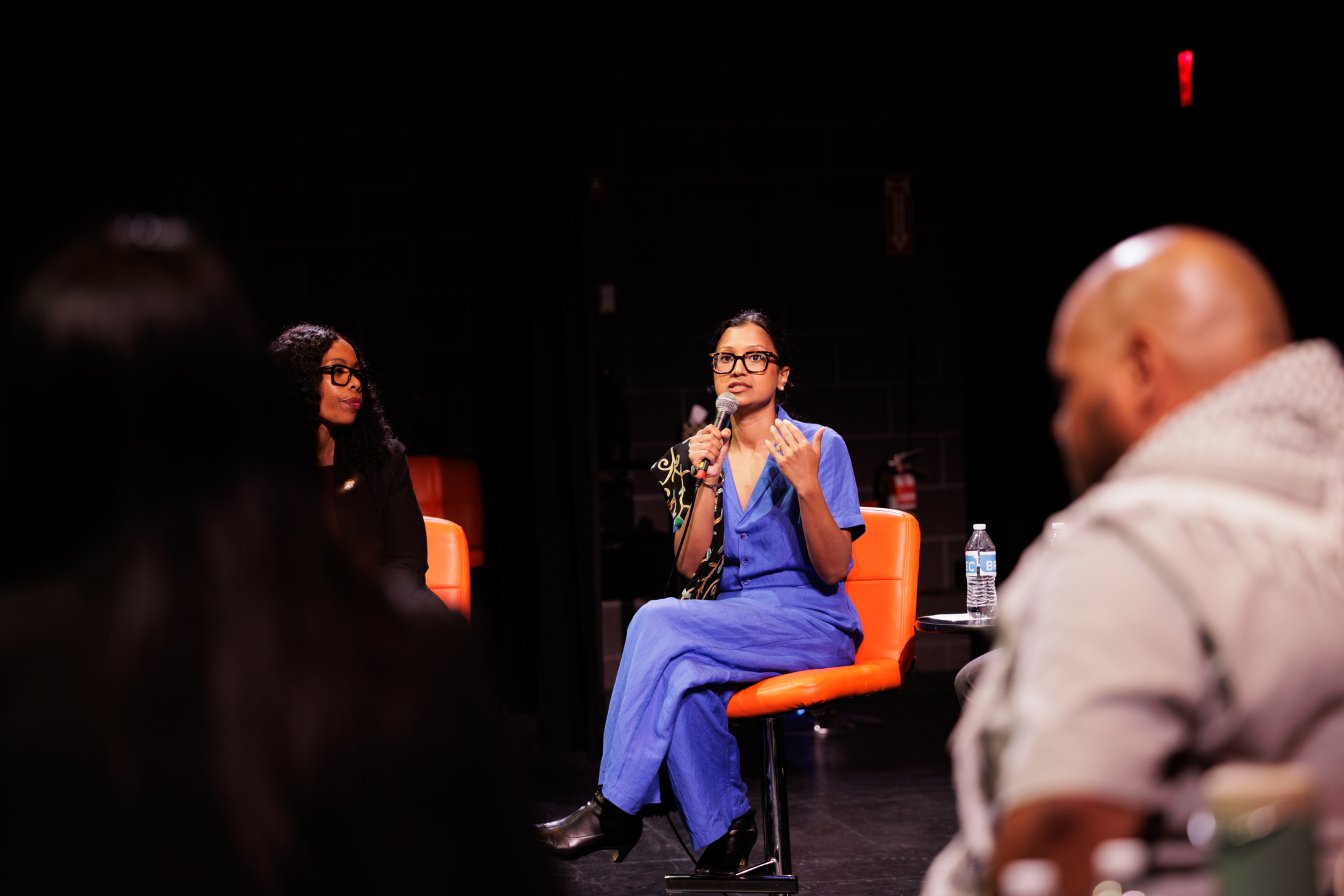 A woman in blue speaks into a microphone while seated onstage with others during a panel discussion.
