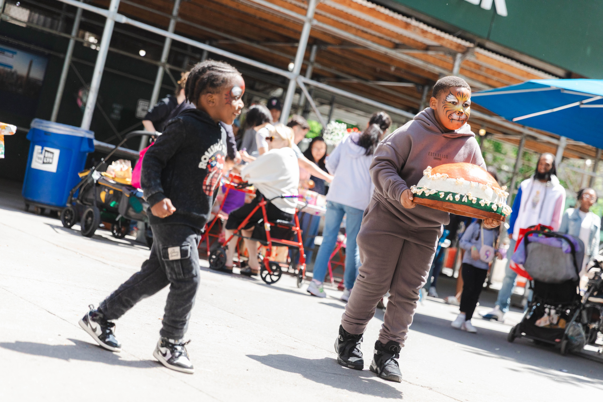 Two children with face paint play outside; one holds a large fake roasted turkey prop. People and tables are visible in the background.