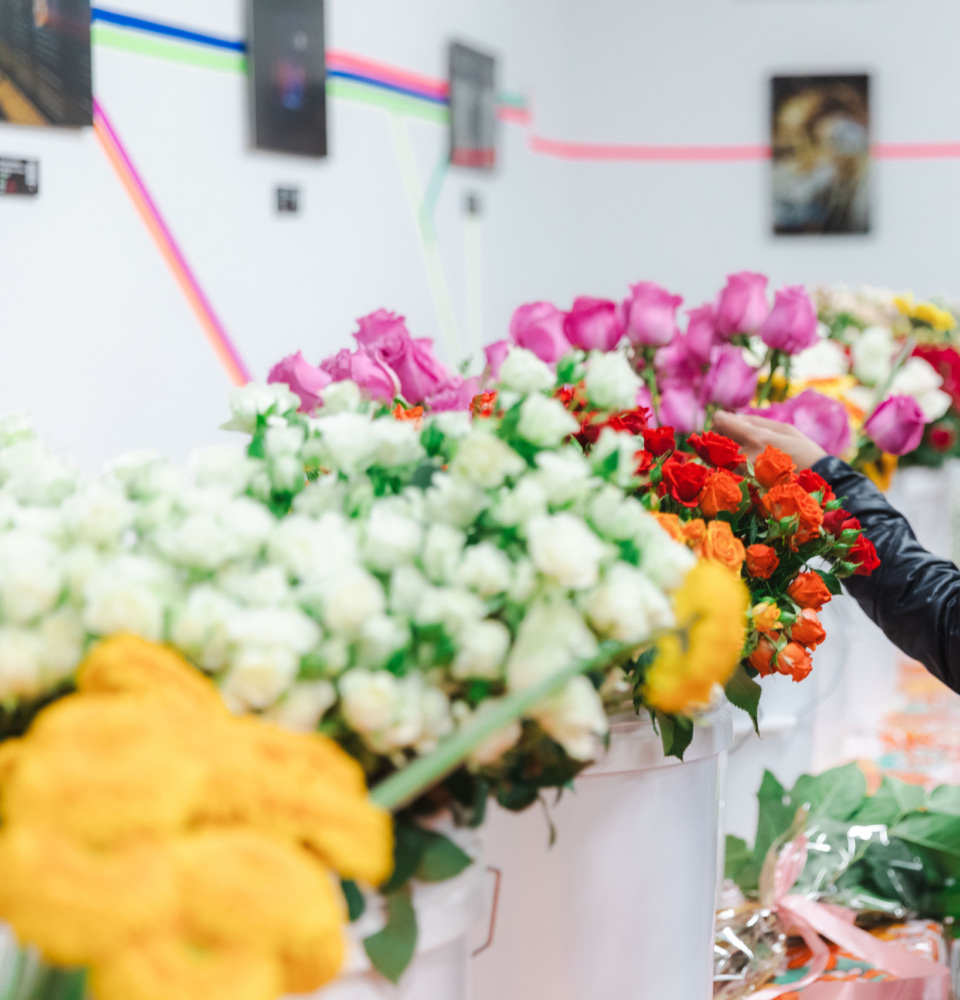 A person wearing a white cap and black jacket selects flowers from several colorful bouquets displayed on a table indoors.