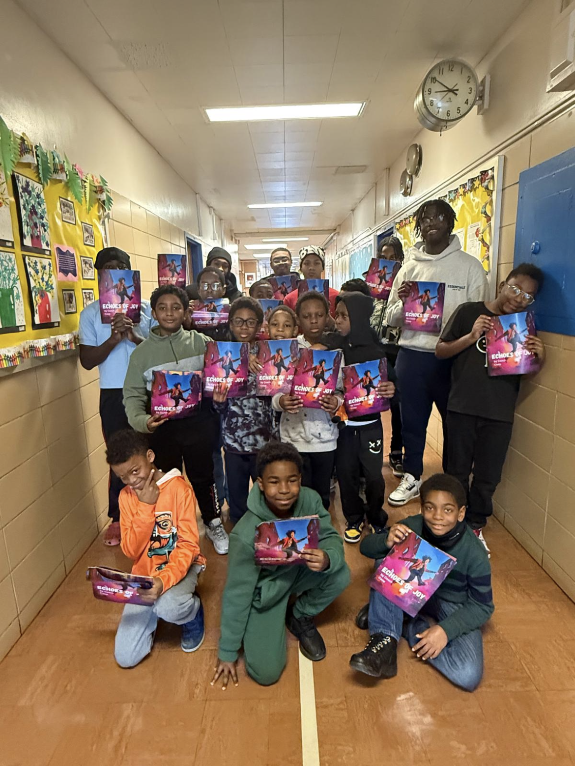 A group of children and adults pose in a school hallway holding up colorful booklets with animated characters on the covers.