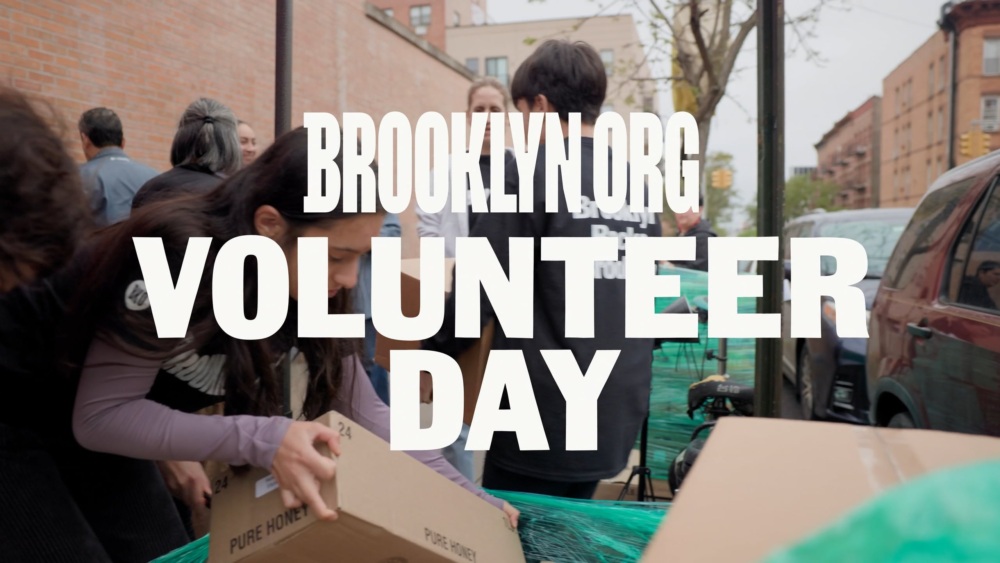 A group of people outdoors handling cardboard boxes, with the text "BROOKLYN.ORG VOLUNTEER DAY" overlaid on the image.