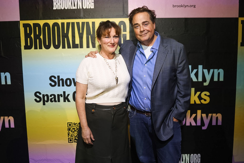 Two people stand together and pose for a photo in front of a colorful Brooklyn-themed event backdrop.