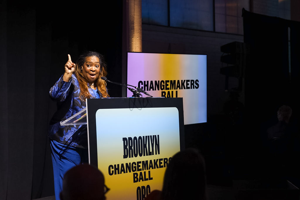 A woman speaks at a podium labeled "Brooklyn Changemakers Ball" with screens in the background displaying the same event name.