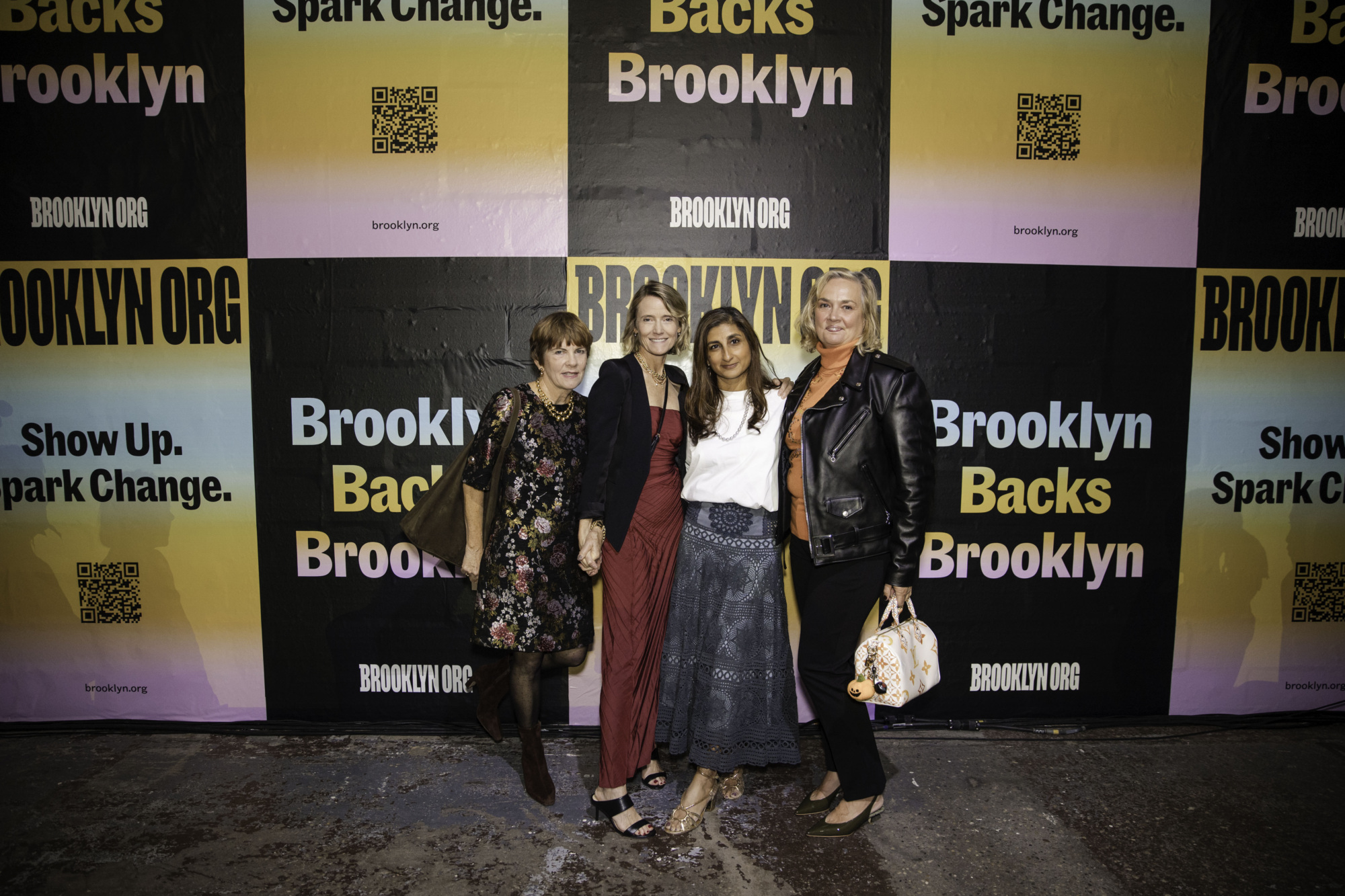 Four women stand together posing for a photo in front of a colorful Brooklyn Backs Brooklyn event backdrop.