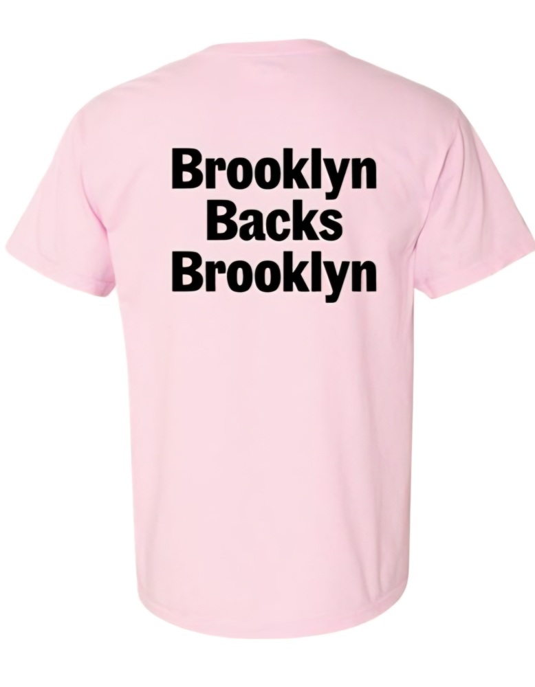 A light pink t-shirt with the words "Brooklyn Backs Brooklyn" printed in bold black letters on the back.