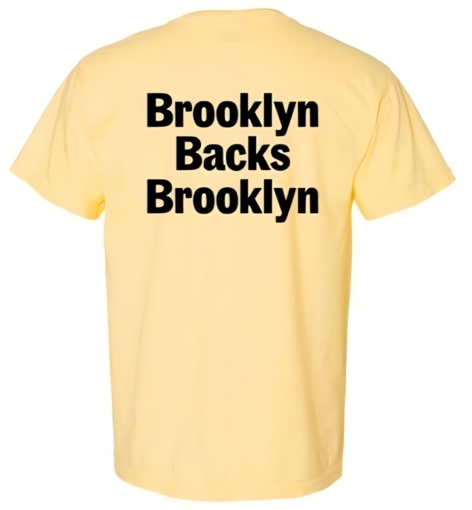 A yellow T-shirt with bold black text on the back that reads "Brooklyn Backs Brooklyn.