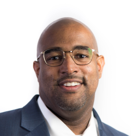 A man wearing glasses and a navy suit jacket over a white shirt, smiling at the camera against a plain white background.