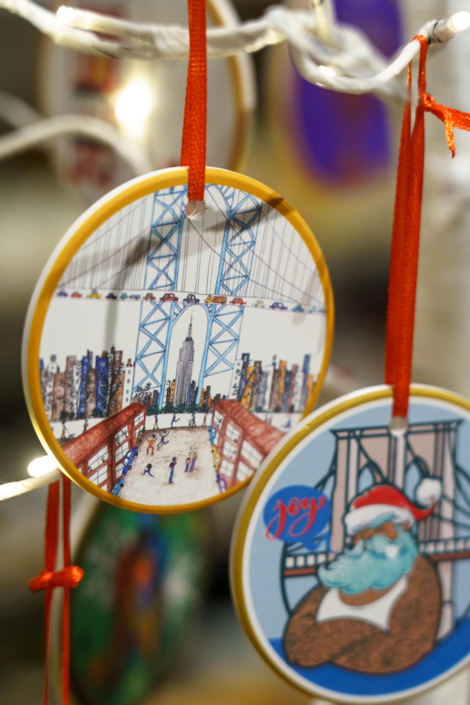 Two round holiday ornaments hang from red ribbons; one depicts a city bridge scene, and the other shows Santa Claus with the word "Joy" beside him.