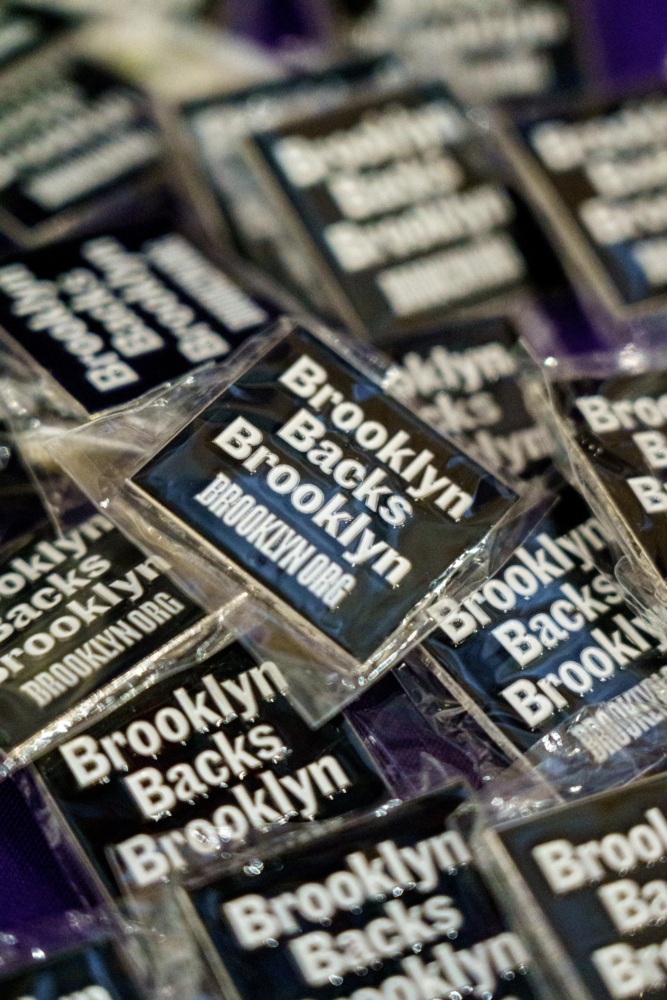 A pile of black and white pins with the text "Brooklyn Backs Brooklyn" and "BROOKLYN.ORG" printed on them, individually wrapped in clear plastic.