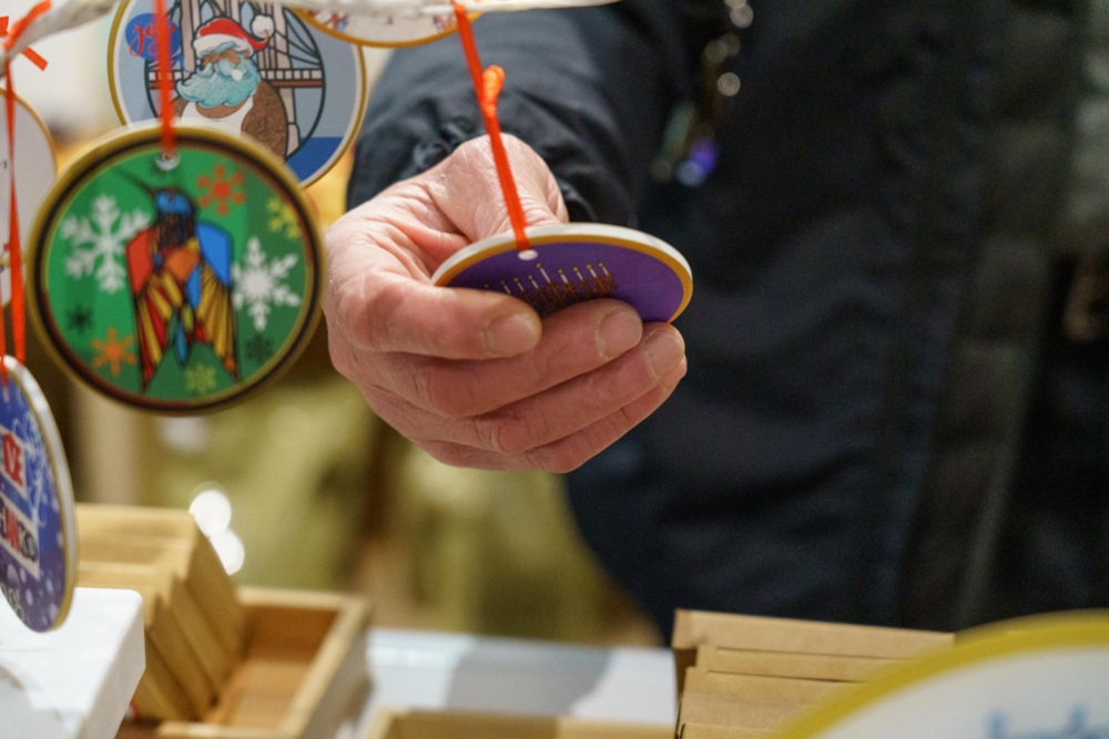 A person holds a round Christmas ornament with a purple background while browsing a display of various ornaments.