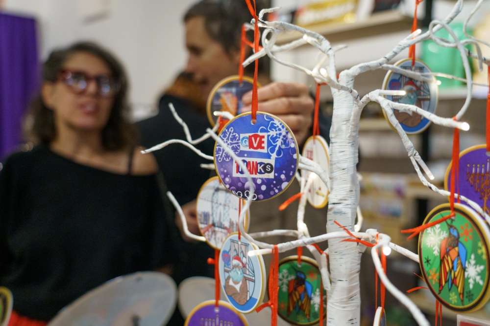 A white decorative tree displays colorful hanging ornaments, one reading "LOVE LINKS," with two people standing in the background.