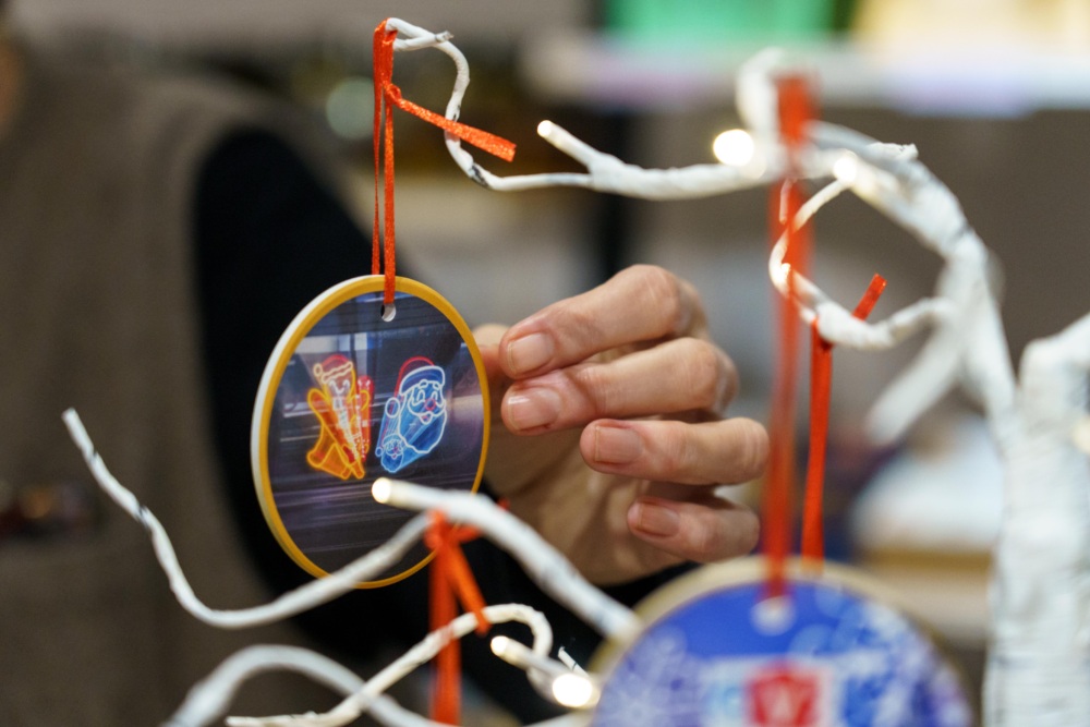 A person hangs a round ornament with neon-style holiday designs on a white, branch-like decoration.