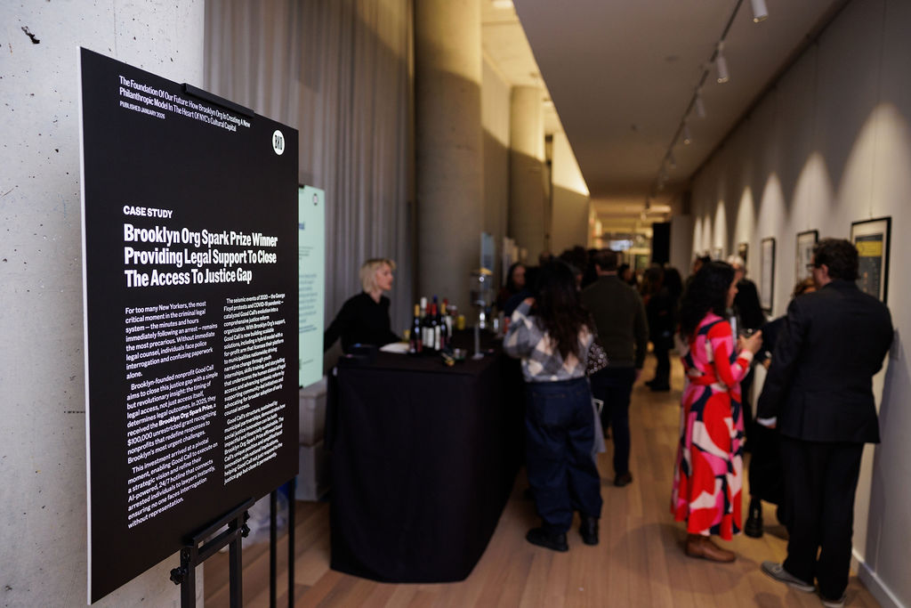 A sign displays case study information at an event, with people socializing and a bar setup visible in a modern hallway.