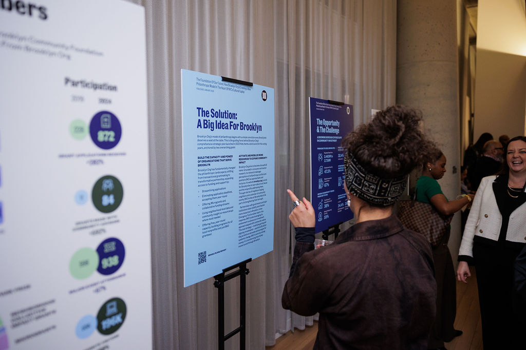 A person reads informational posters displayed on easels at an indoor event, while other attendees interact in the background.