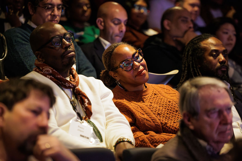 A diverse group of people sits in an auditorium, attentively listening to a presentation.