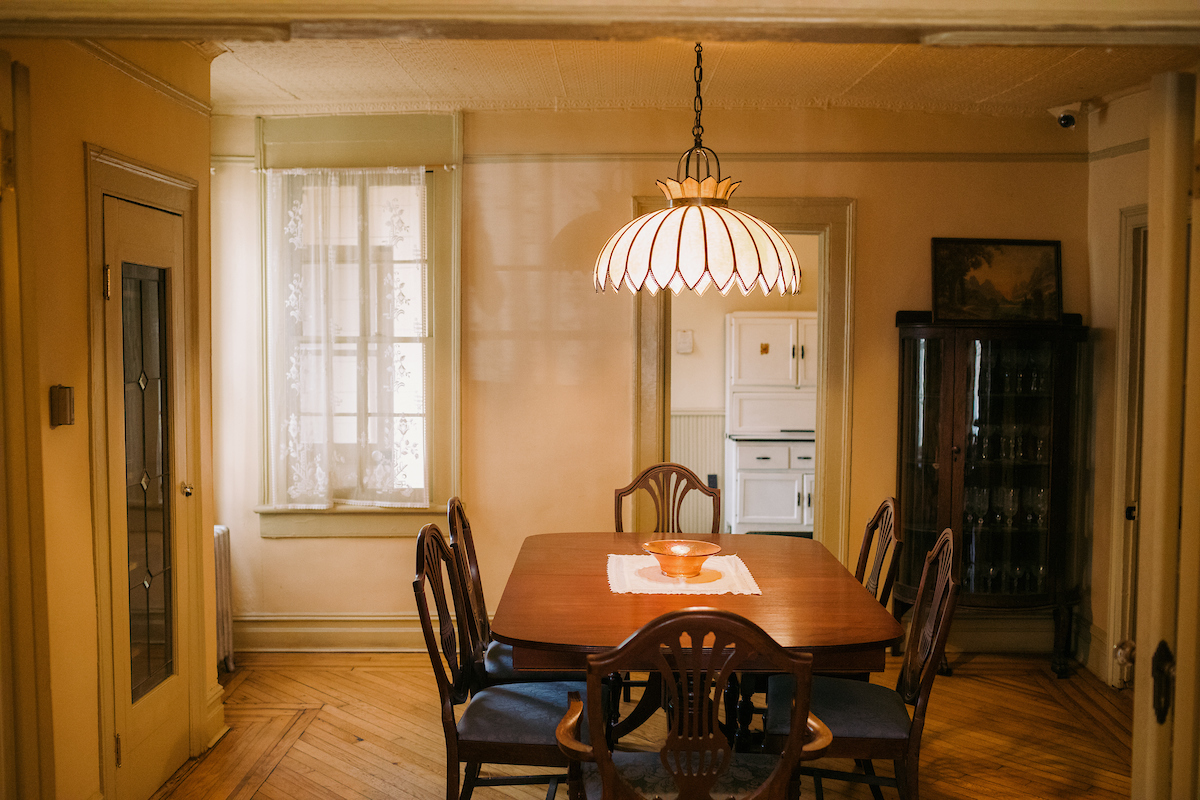 A dining room with a wooden table and six chairs, a hanging light fixture above, and cabinets and a display case in the background.