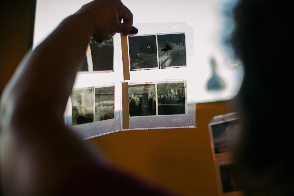 A person holds up photo negatives in plastic sleeves against a light source to examine their contents.