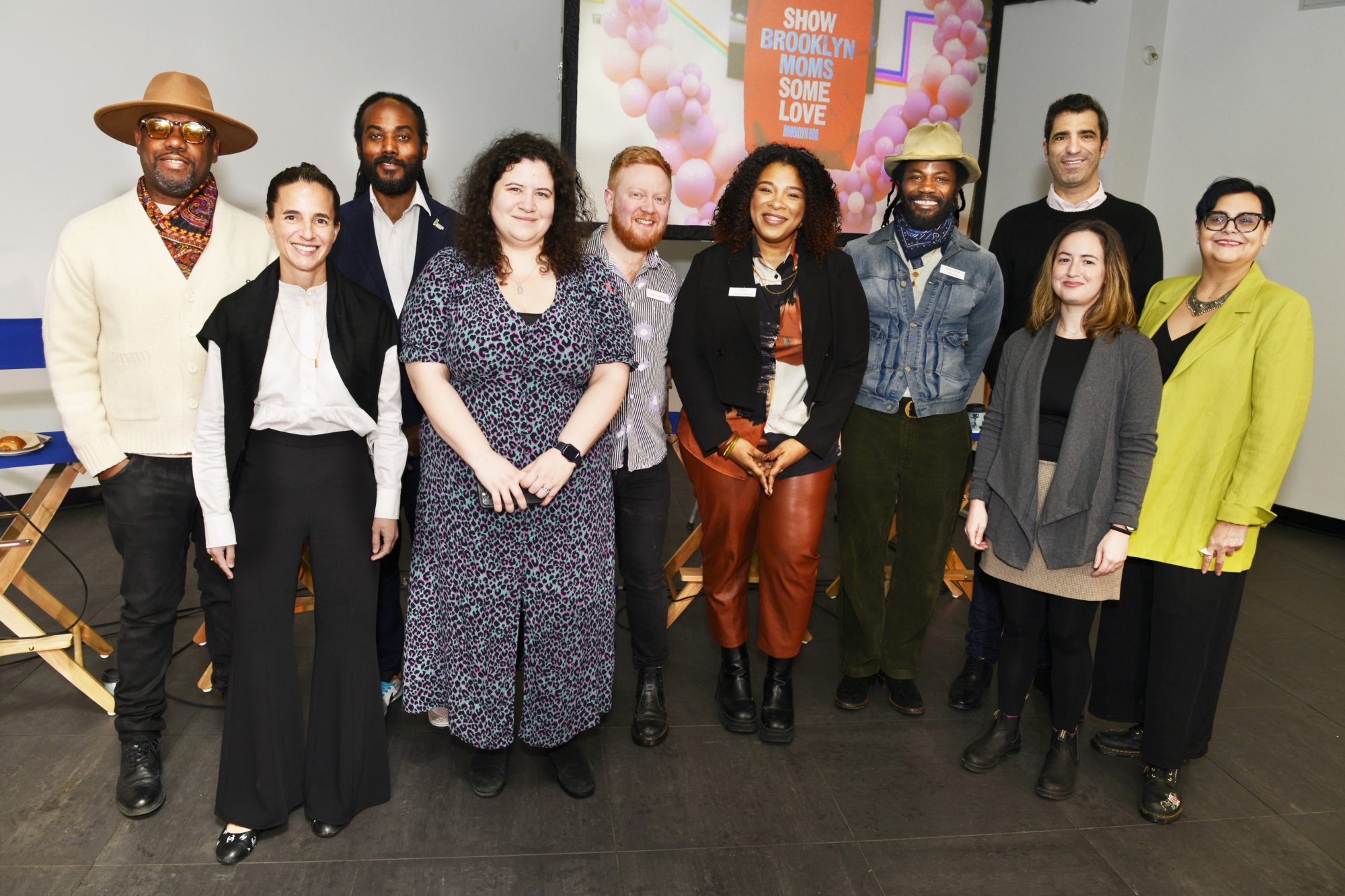 Ten adults stand together indoors, smiling for a group photo in front of a colorful wall display that reads "SHOW BROOKLYN MAKERS SOME LOVE.