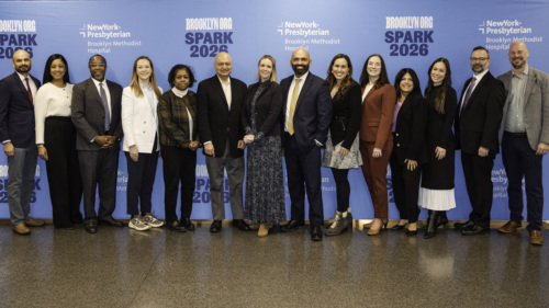 A group of thirteen people stand in front of a blue backdrop with "SPARK 2026" and "NewYork-Presbyterian Brooklyn Methodist Hospital" logos, posing for a group photo.