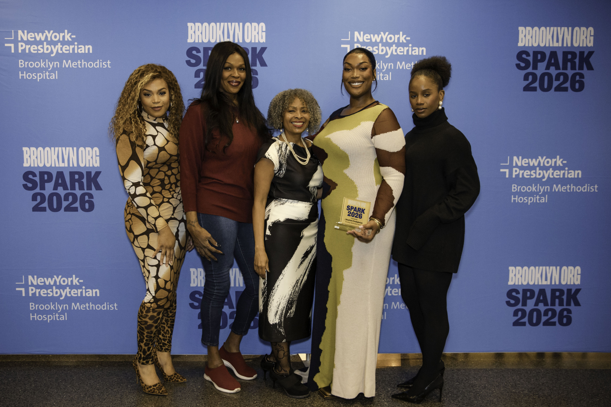 Five women stand together in front of a blue Brooklyn.org SPARK 2026 event backdrop; one woman holds an award plaque.